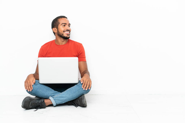 Young Ecuadorian man with a laptop sitting on the floor isolated on white background looking side - Foto, Imagen
