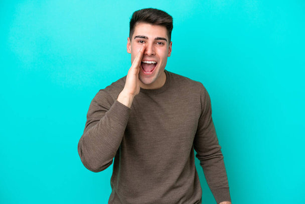 Young caucasian man isolated on blue background shouting with mouth wide open - Photo, Image