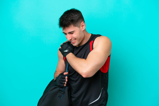 Jonge Kaukasische sportman met sporttas geïsoleerd op blauwe achtergrond die lijdt aan pijn in de schouder voor het hebben van een inspanning - Foto, afbeelding