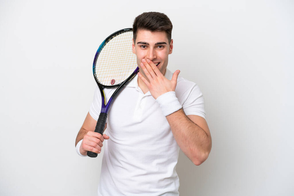 jovem jogador de tênis homem isolado no fundo branco feliz e sorrindo cobrindo boca com a mão - Foto, Imagem