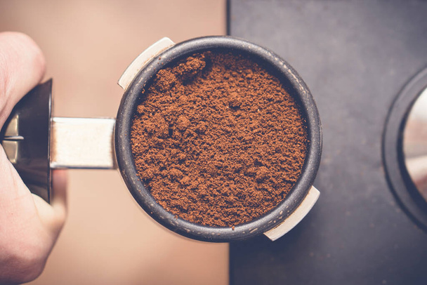 Barista holding portafilter with fresh coffee in hand preparing press coffee with tamper. Close up - Φωτογραφία, εικόνα