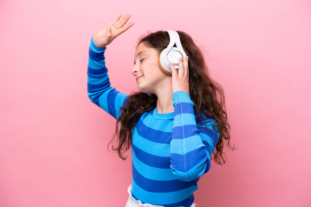 Little girl isolated on pink background listening music and dancing - Foto, Imagem