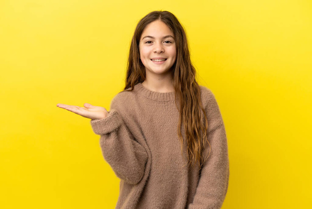 Little caucasian girl isolated on yellow background holding copyspace imaginary on the palm to insert an ad - Foto, Imagen