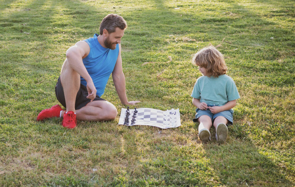 父と息子、小さな男の子チェスをする夏の公園で一緒に屋外で時間を過ごす. - 写真・画像