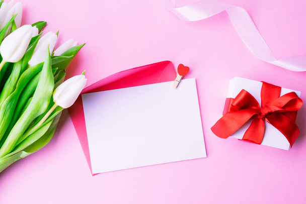Cadeau de la fête des mères. Printemps fleur de tulipe blanche, cadeau avec ruban rouge sur fond plat rose. Valentines, anniversaire, concept de femme ou jour de mariage - Photo, image