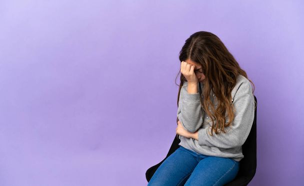 Little caucasian girl sitting on a chair isolated on purple background with headache - Photo, image