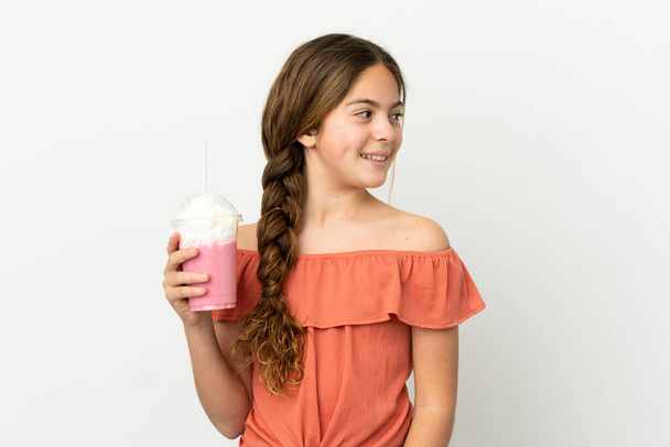 mały kaukaski dziewczyna z truskawkowy milkshake odizolowany na biały tło patrząc z boku - Zdjęcie, obraz