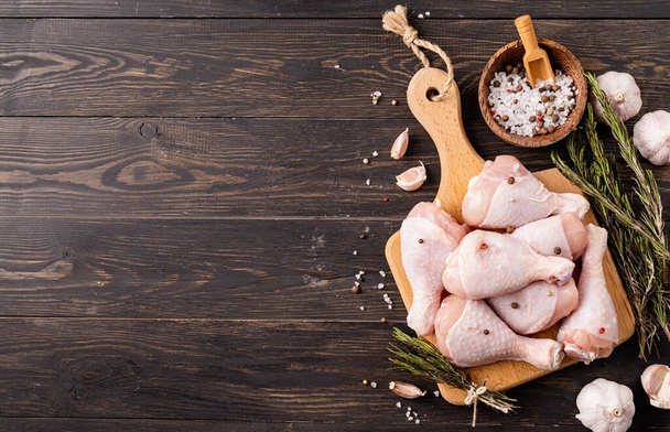 Sliced chicken legs with skin on a cutting board. Dark wooden background. Top view - Foto, afbeelding