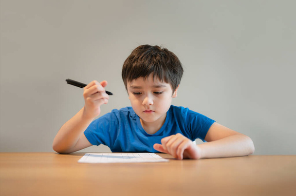 El niño de la escuela usando el dibujo negro del bolígrafo o escribiendo la letra en papel, muchacho joven que hace la tarea, niño con las notas de la escritura del bolígrafo en hoja de papel durante la prueba del pupilo de lesson.Cute que hace, concepto de la educación en el hogar - Foto, Imagen