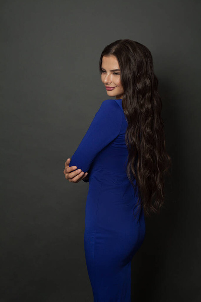 Brunette woman with curly hairstyle wearing classic stylish blue dress on gray background - Φωτογραφία, εικόνα