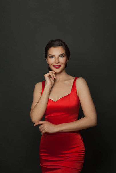 Glücklich lächelnde Frau mit Make-up in erstaunlichem roten Kleid feiert Neujahrsparty auf schwarzem Hintergrund. - Foto, Bild