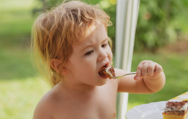 Baby eating cake. Cute child eats delicious outside. - Photo, image