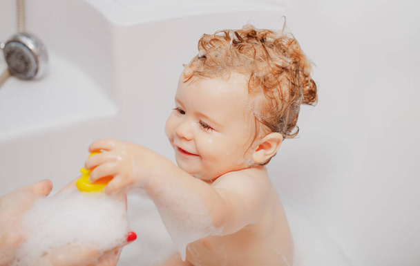 Bathing baby. Happy kid with soap foam on head. Child bubble bath. - 写真・画像