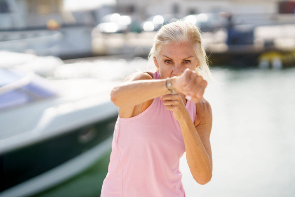 Mature woman doing shadow boxing outdoors. Senior female doing sport in a coastal port - Photo, Image