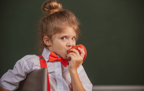 Kleine scholier leerling in de klas, eet appel op school. Grappige kinderen gezicht close-up. - Foto, afbeelding