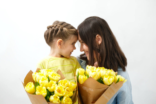 portrait of smiling mother and daughter with bouquet of yellow tulips looking at each other, unconditional love, mother's day concept - Zdjęcie, obraz