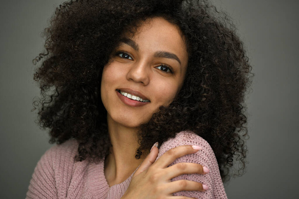 Nahaufnahme Porträt einer schönen jungen afrikanisch-amerikanischen Frau mit Afro-Haaren, lächelnd, die in die Kamera blickt. Studioaufnahme auf grauem Hintergrund. - Foto, Bild
