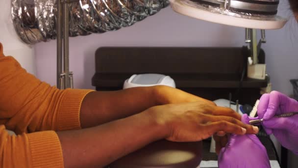 Vrouwelijke meester in beschermende handschoenen maakt manicure aan zwarte man in een salon in close-up - Video