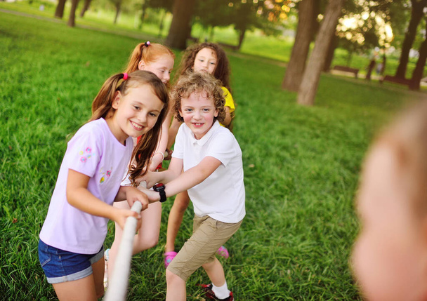 group of preschool children - boys and girls compete in a tug of war against the background of a park and greenery. - Фото, изображение