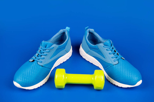 sporty blue sneakers pair with dumbbell on blue background, sport accessory - Fotografie, Obrázek