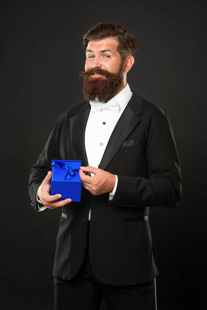 cheerful man in tuxedo bow tie formalwear on black background with box. birthday - Zdjęcie, obraz