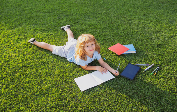 Little boy writing on notebook in summer sunset light. - Foto, imagen