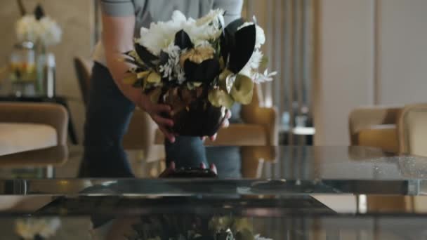 Pokojówka kładzie wazon ze świeżymi kwiatami na stole.. - Materiał filmowy, wideo