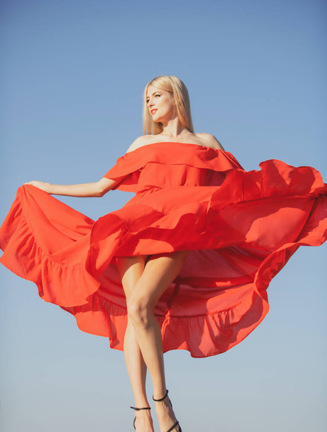 Woman in red dress movement on sky. Beautiful girl in stylish fashion clothes in summer. Fashion woman posing outdoors. - Fotó, kép