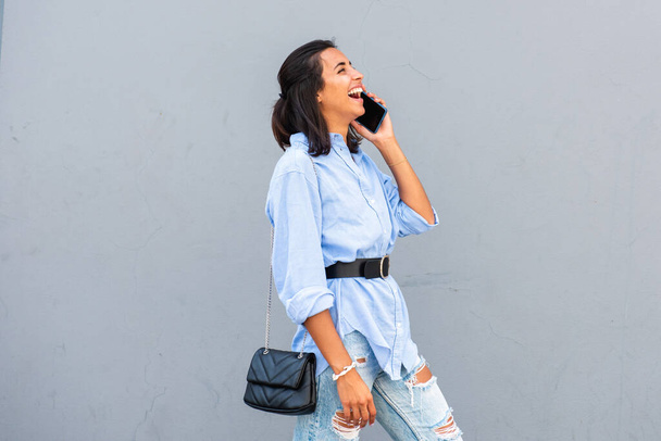 Side muotokuva nuori nainen nauraa puhuessaan matkapuhelimen harmaa seinä - Valokuva, kuva