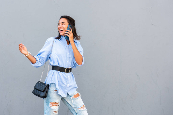 Muotokuva onnellinen nuori nainen puhuu matkapuhelimen kanssa ja kääntyy ympäri harmaalla taustalla  - Valokuva, kuva