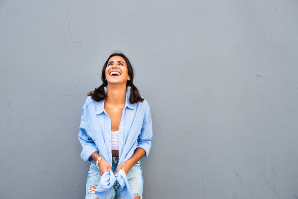 Portrét krásné smějící se mladé ženy stojící na šedém pozadí vzhlížející - Fotografie, Obrázek