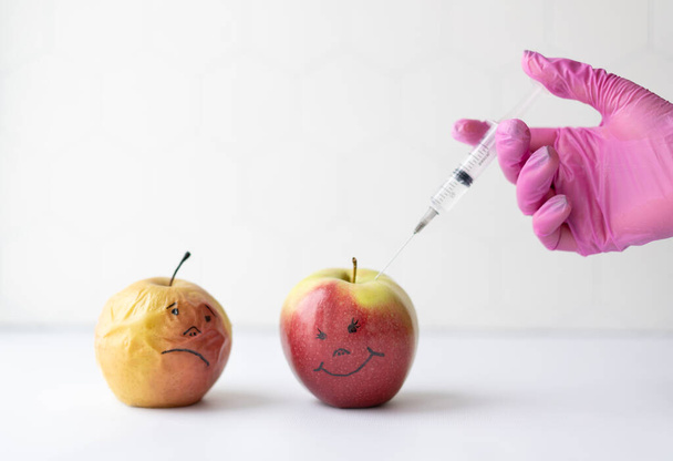 Het concept van schoonheidsbehandelingen en verjonging. Elastische en verschrompelde appels en een spuit met een geneesmiddel voor injectie.  - Foto, afbeelding