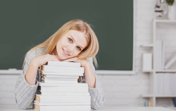 Close up portrait of happy attractive young woman student with books on blackboard in classroom. - Foto, immagini