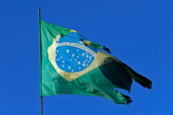 Bandera brasileña desgarrada en fuerte viento y cielo azul
 - Foto, Imagen