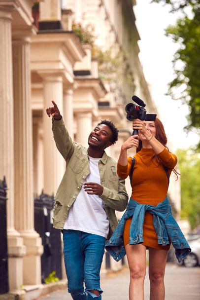 Young Couple Travelling Through City Together Vlogging To Video Camera On Handheld Tripod - Foto, imagen