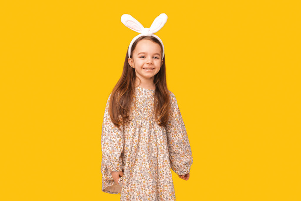 Маленька дівчинка в сукні і роки кролика готова до Великодня. Студійний знімок на жовтому тлі
. - Фото, зображення
