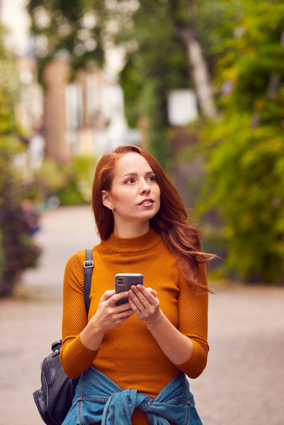 Female Vlogger Or Social Influencer Walking Through City Street Looking At Mobile Phone - Fotoğraf, Görsel