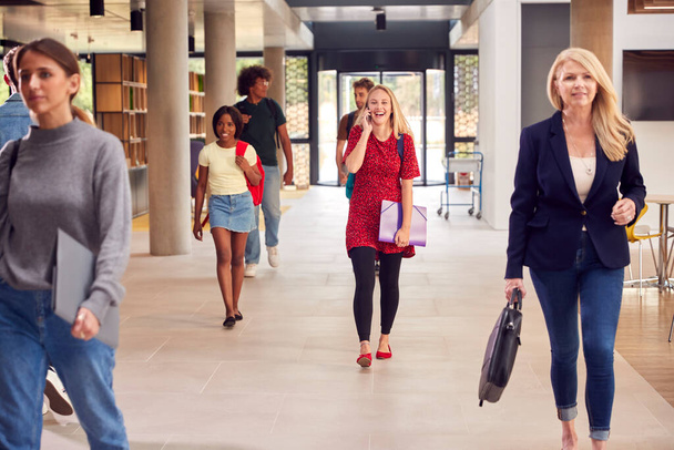 Female Student Talks On Mobile Phone As She Walks Through Busy University Or College Building - Foto, Imagen