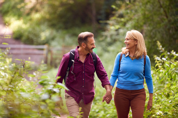 Mature Loving Couple In Countryside Hiking Along Path Through Forest Together Holding Hands - Photo, Image