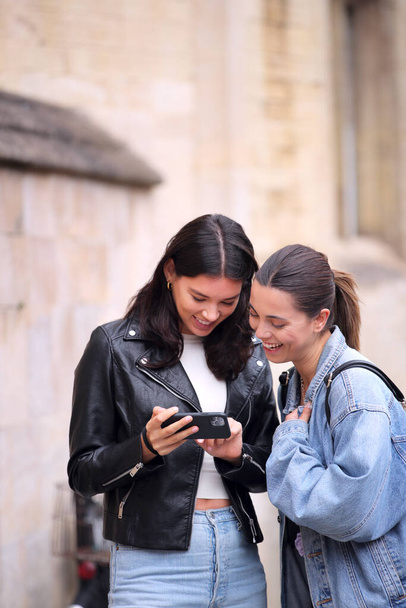 Same Sex Female Couple Sightseeing Looking At Mobile Phone And Walk Around Oxford UK Together - Foto, imagen