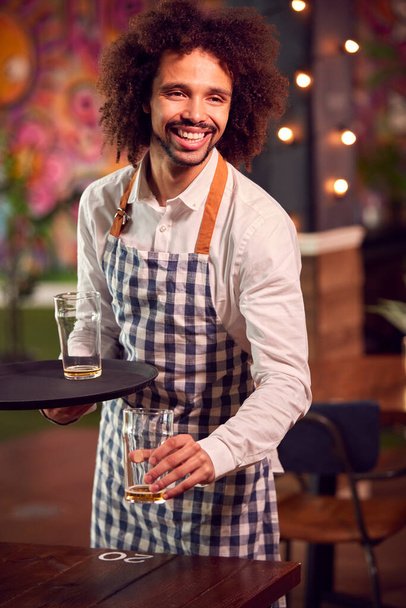 Portrait Of Smiling Male Server Clearing Table In Cool Bar Or Club - 写真・画像
