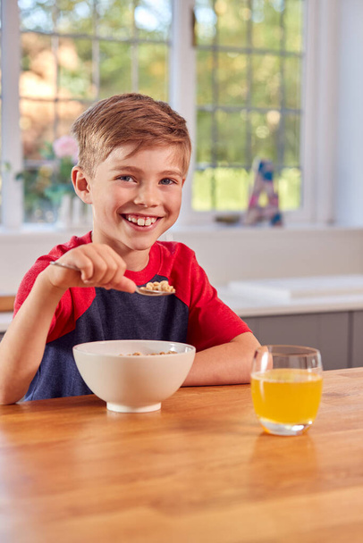 Retrato de menino em casa comendo tigela de cereais do café da manhã no balcão da cozinha - Foto, Imagem