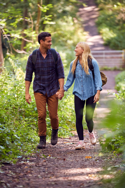 Loving Couple In Countryside Hiking Along Path Through Forest Together Holding Hands - Foto, imagen