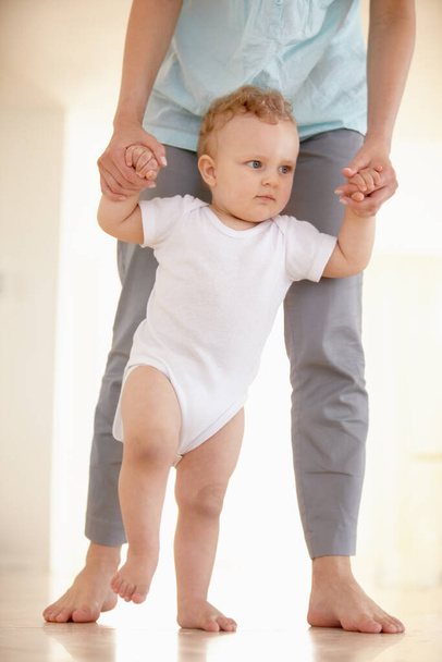 Tomando sus primeros pasos.... Imagen recortada de las piernas de un bebé caminando con un padre apoyando desde atrás. - Foto, Imagen