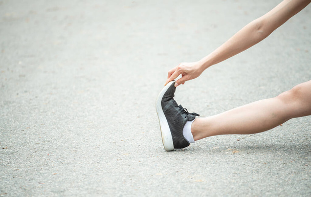 Ausgeschnittene Aufnahme einer Läuferin beim Dehnen und Aufwärmen ihrer Beine vor dem Laufen. Der Vorteil des Dehnens kann die Beweglichkeit steigern und das Verletzungsrisiko verringern. - Foto, Bild
