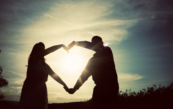 Silhouette di coppia amorevole che si tiene per mano a forma di cuore sopra o
 - Foto, immagini