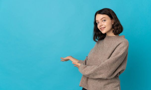 Teenager Ukrainian girl isolated on blue background extending hands to the side for inviting to come - Фото, изображение