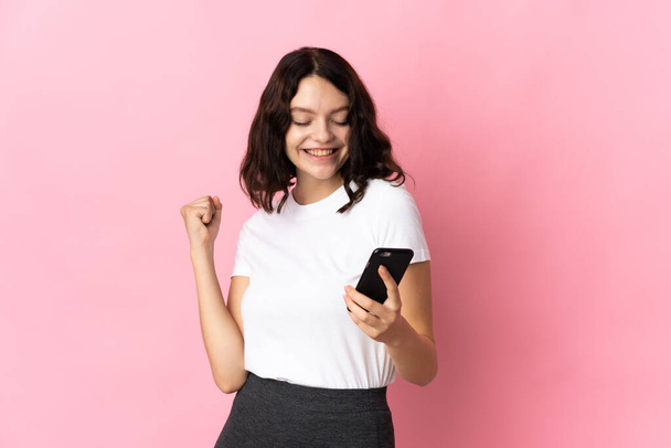 Teenager Ukrainian girl isolated on pink background with phone in victory position - Zdjęcie, obraz