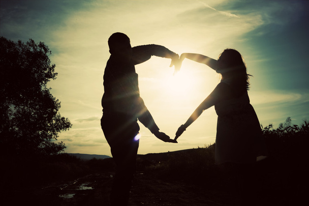 Silhouette di coppia amorevole che si tiene per mano a forma di cuore sopra o
 - Foto, immagini