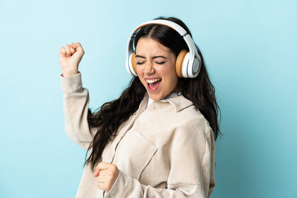 Young caucasian woman isolated on blue background listening music and dancing - Photo, image